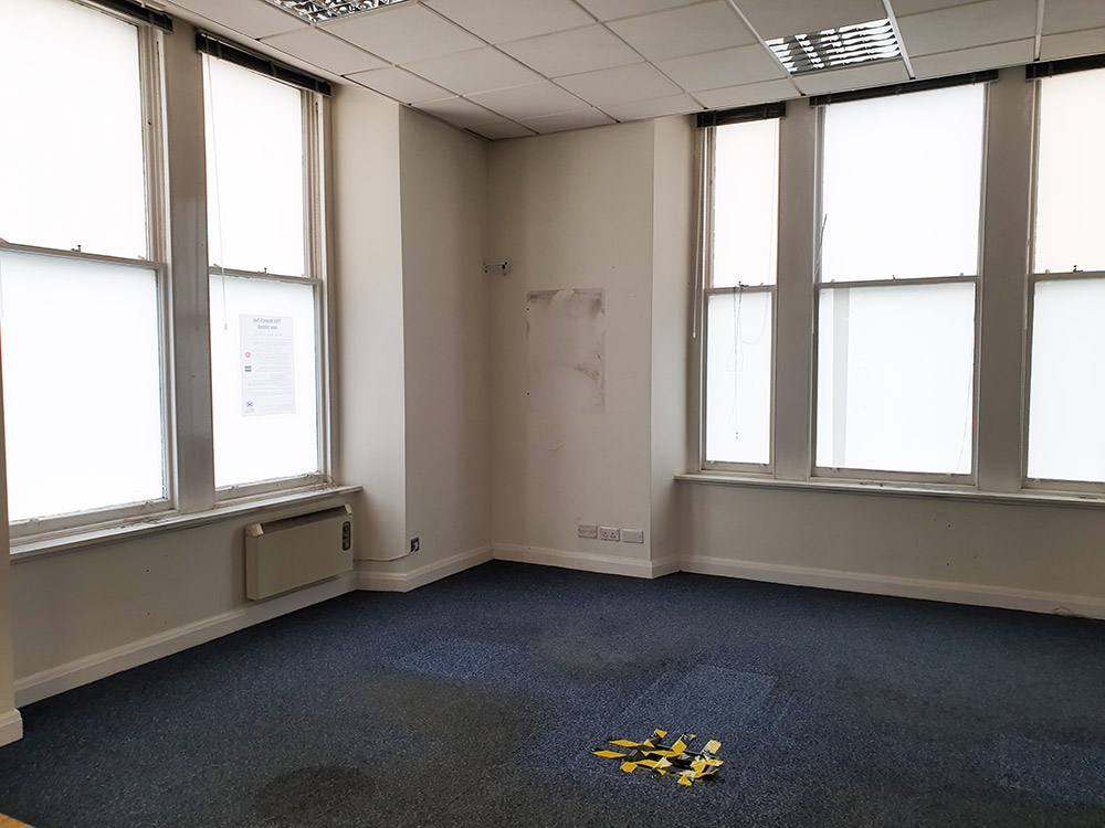 Empty room with five large windows and stained blue carpet. Former Bank of Scotland