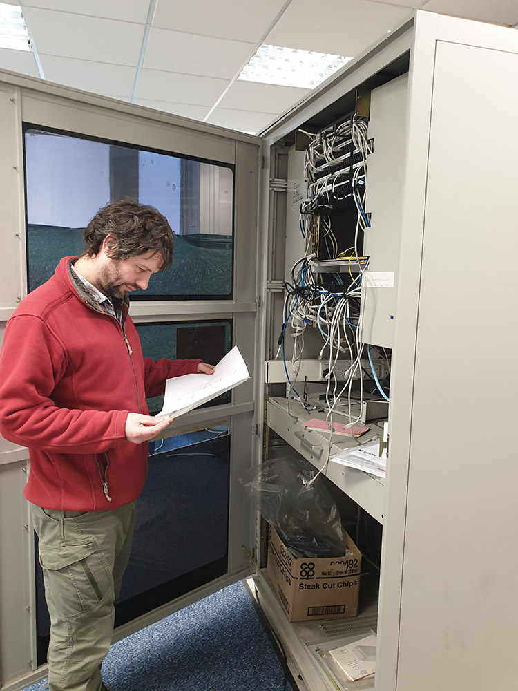 Man reading papers standing in front of large metal box with wires inside